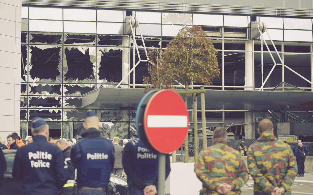 Police and soldiers from the Belgian Army stand in front of blown out windows at Zaventem Airport in Brussels. Photo: AP Photo\/Yorick Jansens