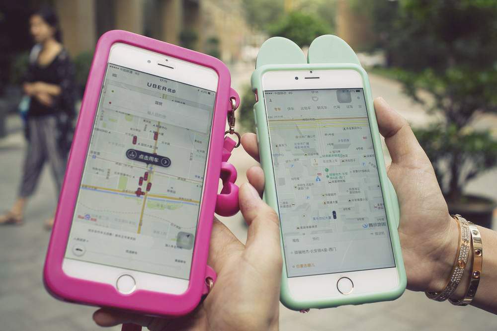 Women holding their smartphones show the ride-hailing apps Uber Technology Ltd., left, and Didi Chuxing. Photo: Andy Wong/AP Photo