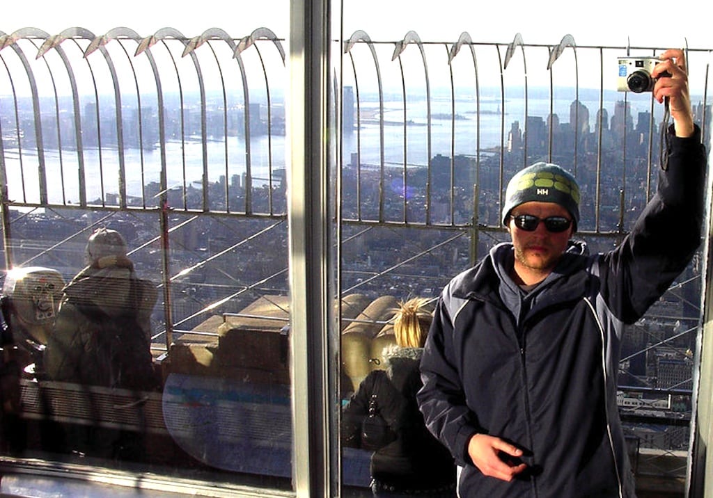Photographer takes a self-portrait using a mirror in the Empire State Building observatory in 2005. Downtown Manhattan and the Hudson River are in the background. 