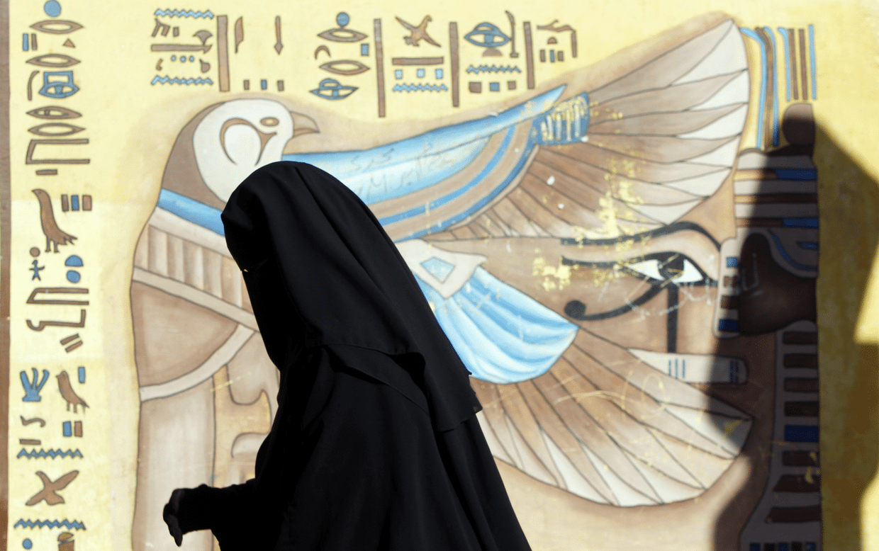 A woman wearing a full veil (niqab) queues near a hieroglyphic mural outside a polling centre as she waits to vote during the final stage of a referendum on Egypt's new constitution in El Dokki district of greater Giza, south of Cairo. 