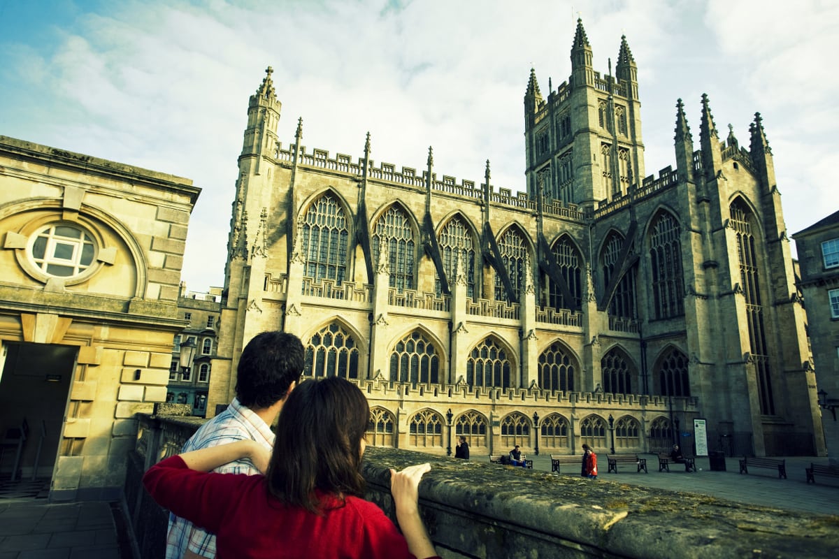 A couple looking up at the historic Bath Abbey, the last great gothic church in England, from the Roman Baths in Somerset. 
