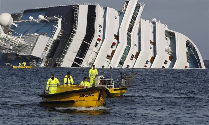 Oil recovery workers pass in front of the Costa Concordia cruise ship which ran aground off the west coast of Italy at Giglio island and is now half-submerged and threatening to slide into deeper waters January 22, 2012. 
