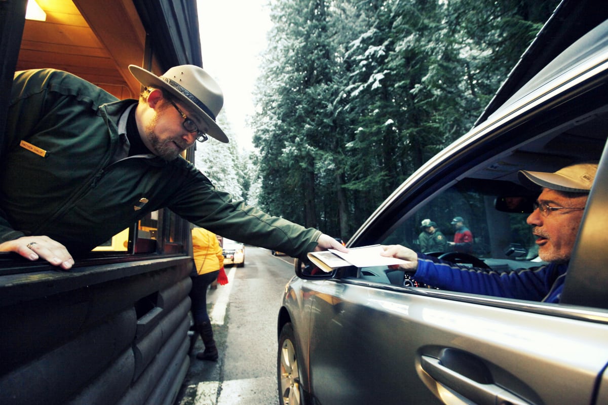 Federal government sequestration in 2013 reduced demand for business and government travel, and shuttered national parks. In this Jan. 7, 2012 file photo, Mount Rainier  National Park Ranger Matt Chalup, left, hands park information to one of the first visitors to the park at the Nisqually entrance near Ashford, Wash.  