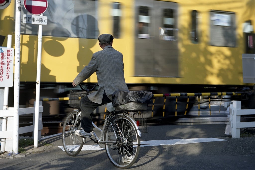 A cyclist waits at a railroad crossing as a train operated by Seibu passes by. 