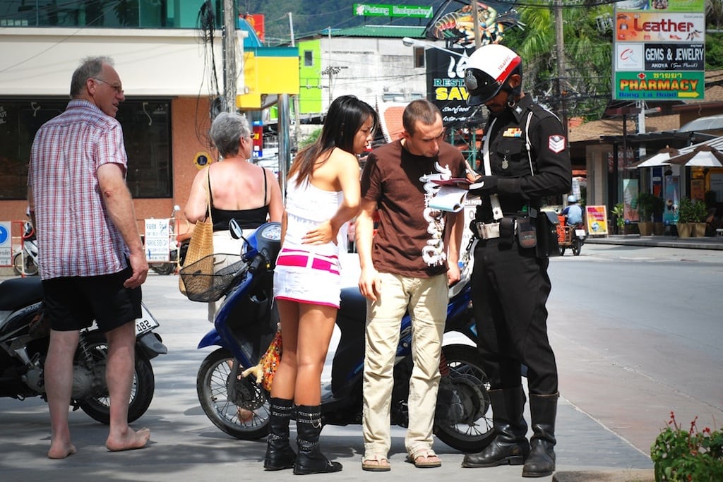 A Phuket police officer hands out tickets to tourists for riding bikes without helmet. 