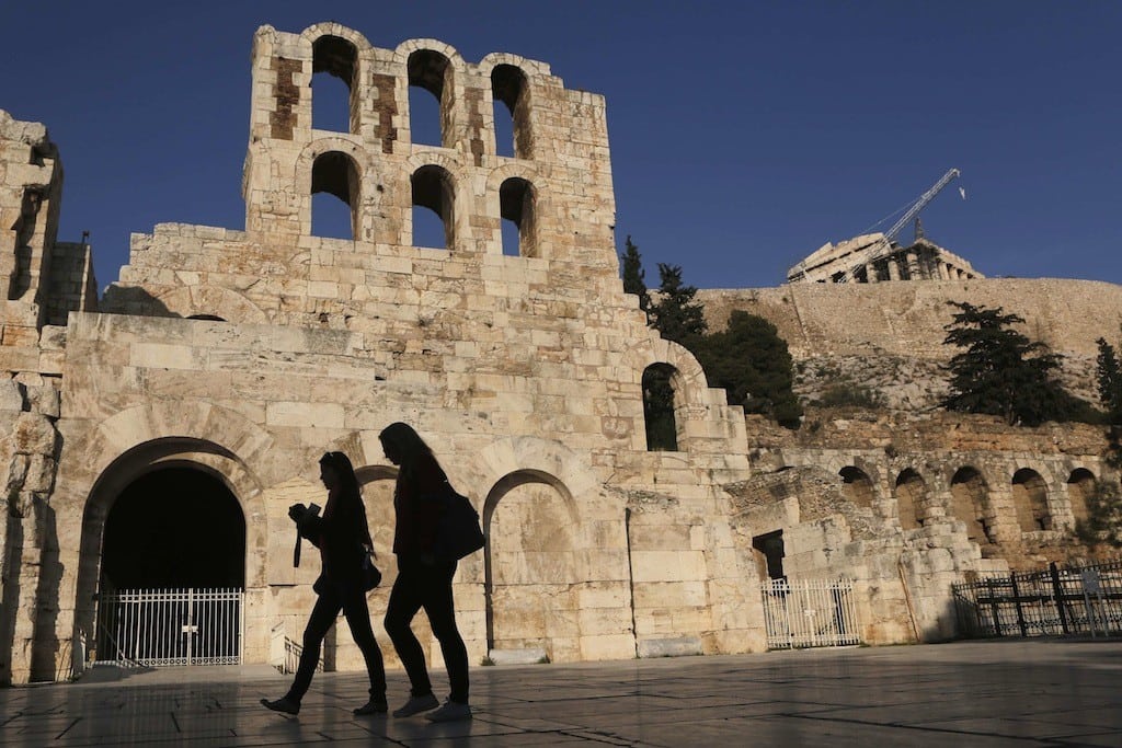 Women walk outside of the ancient Herodes Atticus theatre as the Parthenon temple is seen in the background in Athens. 