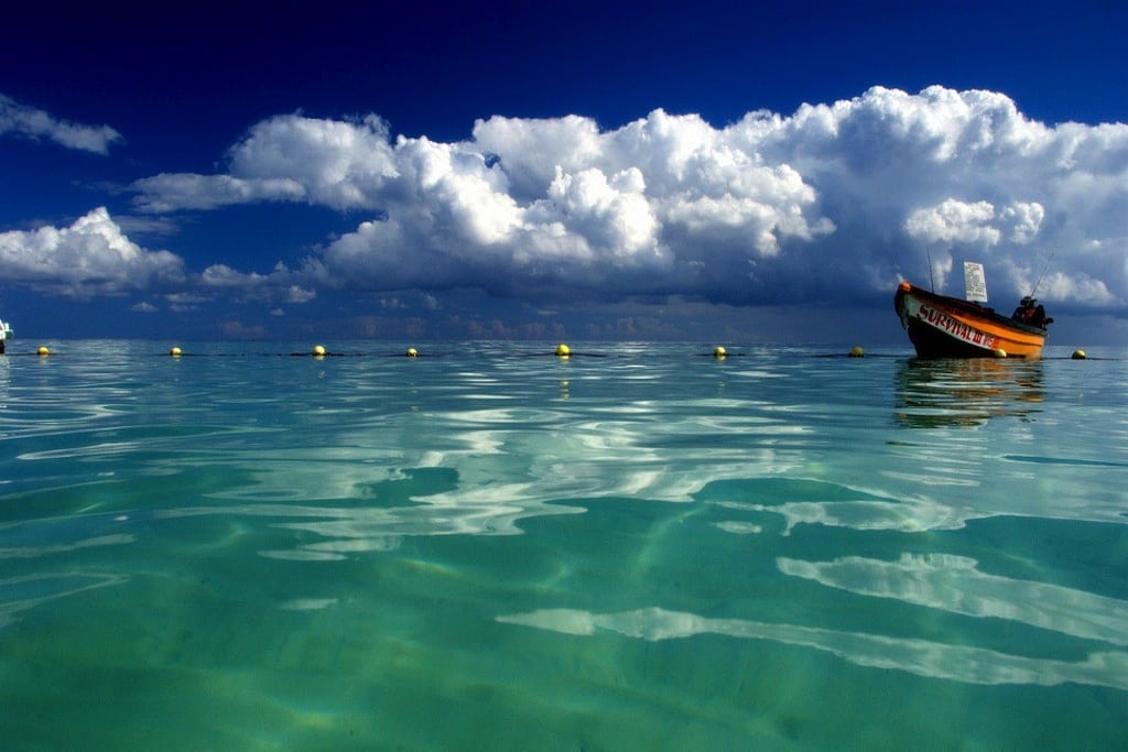 A photographer waits in the water for tourists to come for a trip on his fishing boat. 