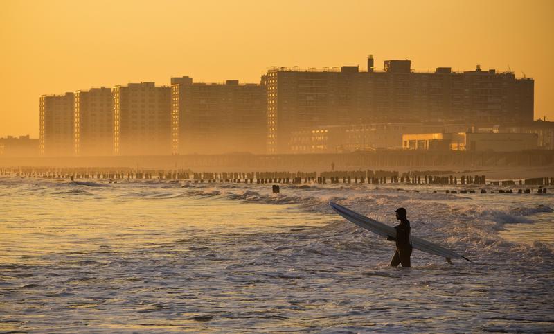 Surfer walks out into the ocean at Rockaway Beach in the Queens Borough of New York.
