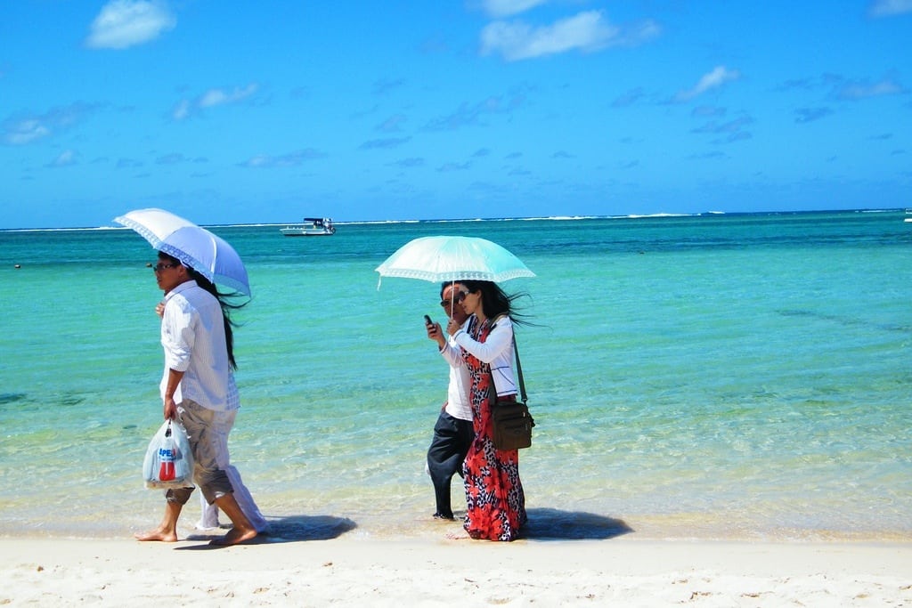 Asian tourists shade themselves from the midday Mauritian sun as they stroll along the beach. 