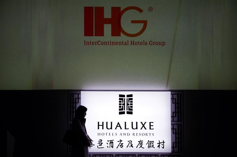 A woman stands near an illuminated sign for Hualuxe Hotels and Resorts during its official launch inside the Forbidden City in Beijing. 
