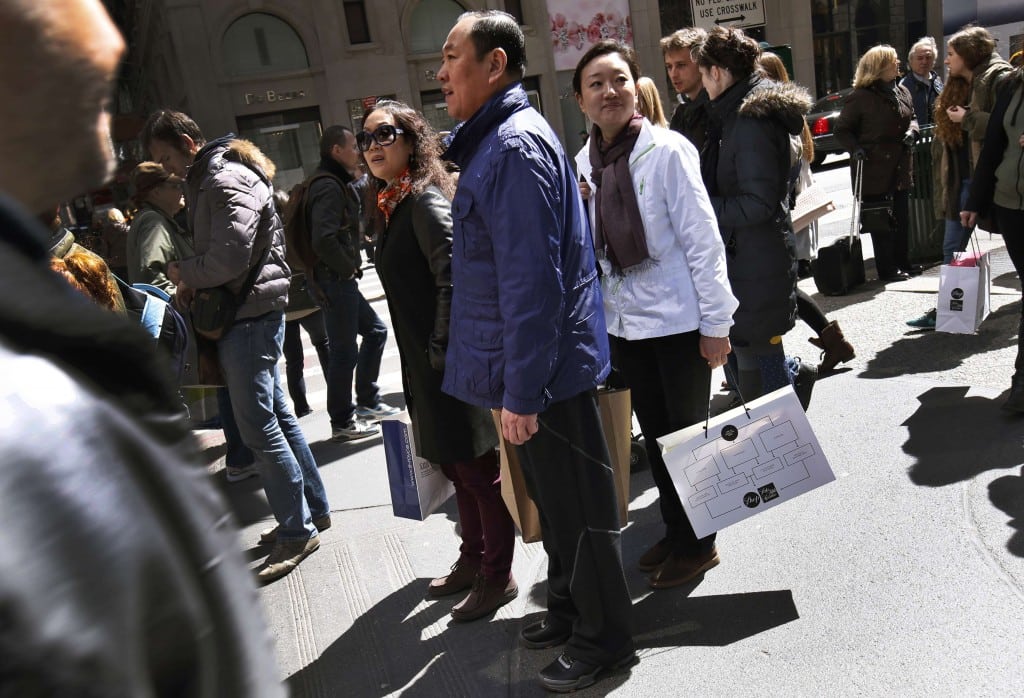 Chinese shoppers stand with shopping bags on a sidewalk along 5th Avenue in New York. 