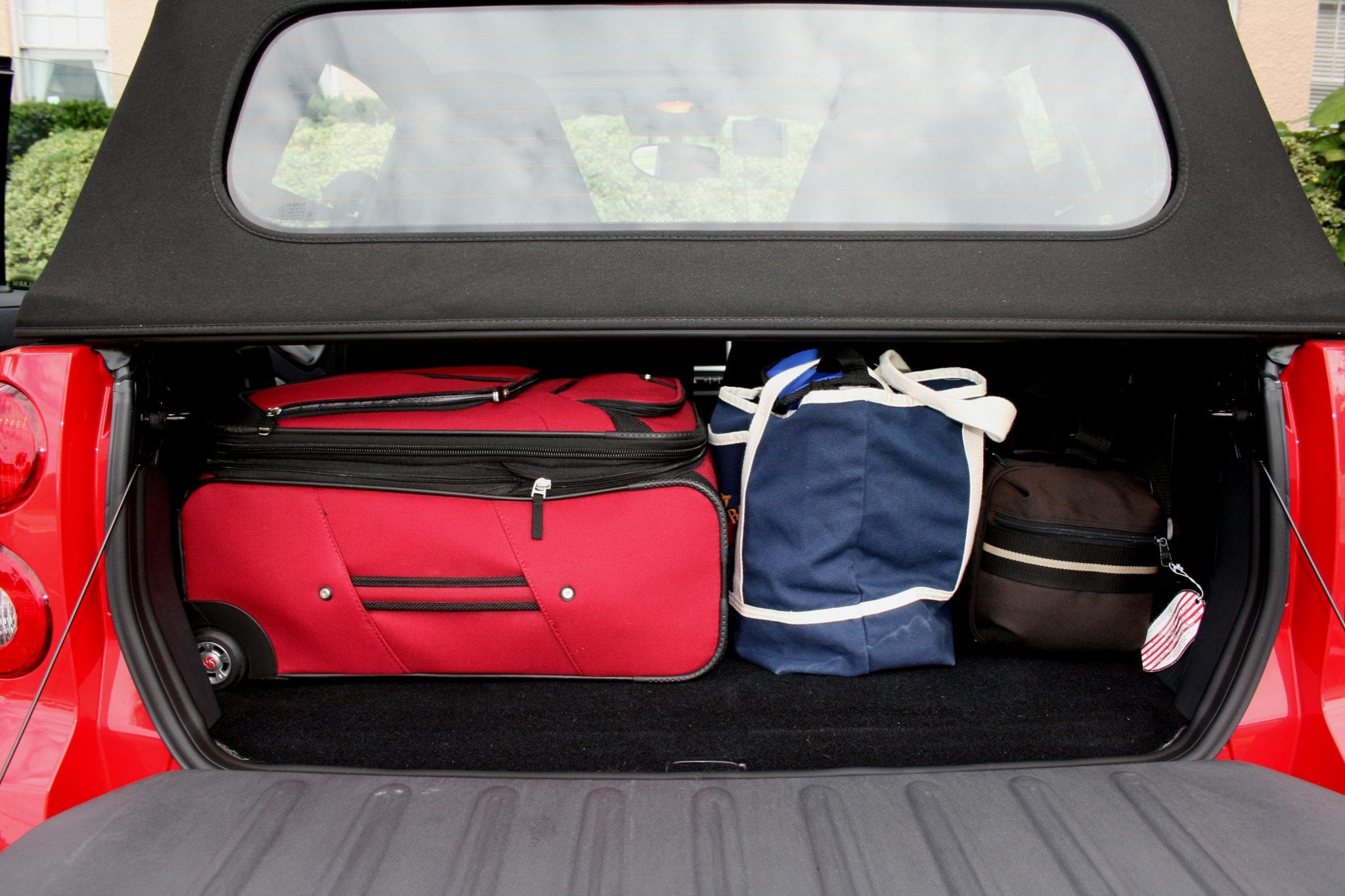 A 22-inch roll-aboard suitcase, a full totebar and a camera bag packed in a car. 