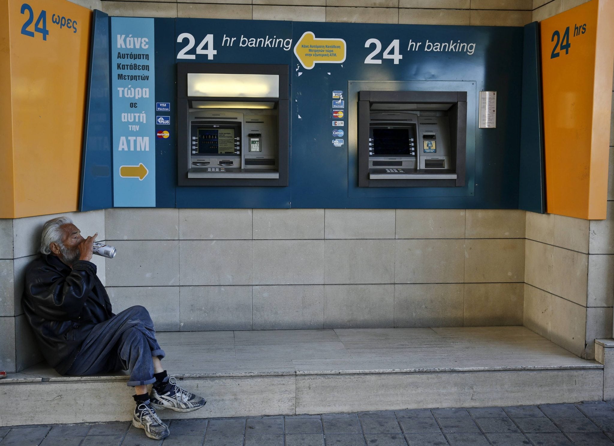 A man drinks beer near ATMs outside a branch of the Bank of Cyprus in Nicosia. 