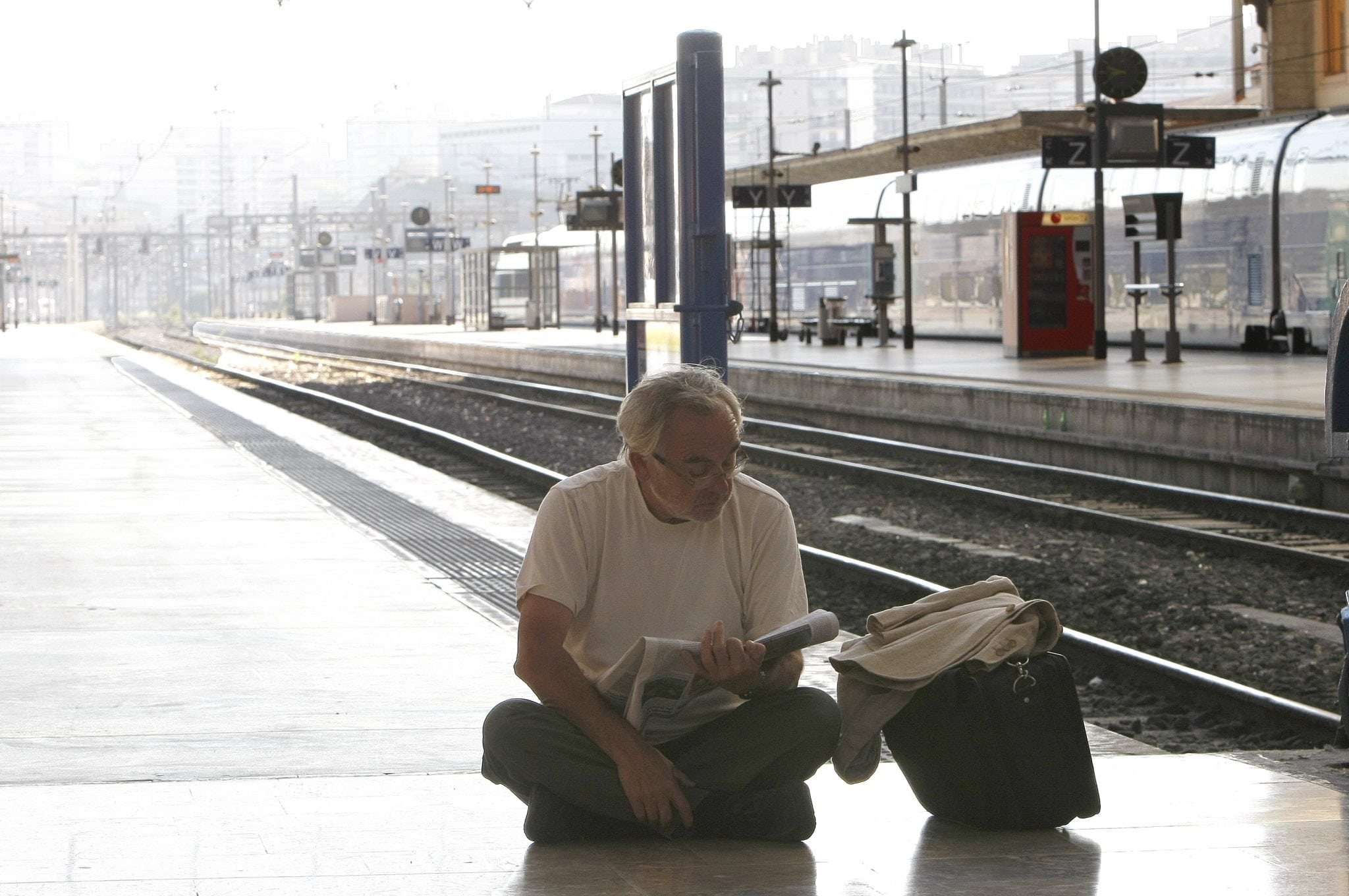 Passenger sits on the ground and reads a newspaper in front of an empty platform, at Saint-Charles railway station, in Marseille, southern France, Thursday June 13, 2013, as French rail workers are on strike to protest a reorganization of the national rail and train companies. 