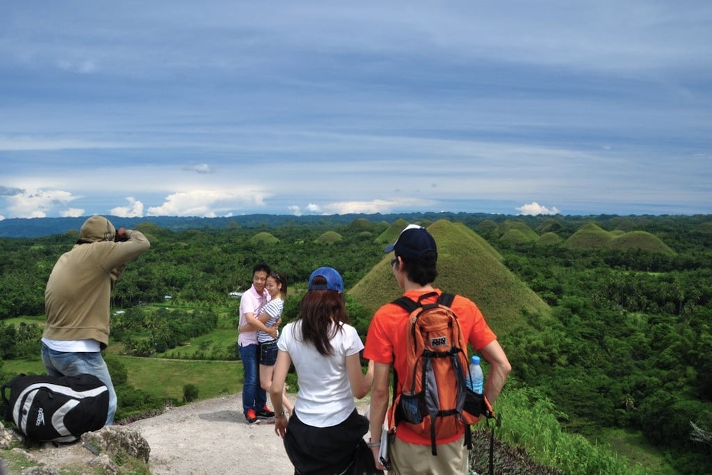 A photographer snaps a photo of a couple while another pair looks on at the "chocolate hills" of Philippines. 
