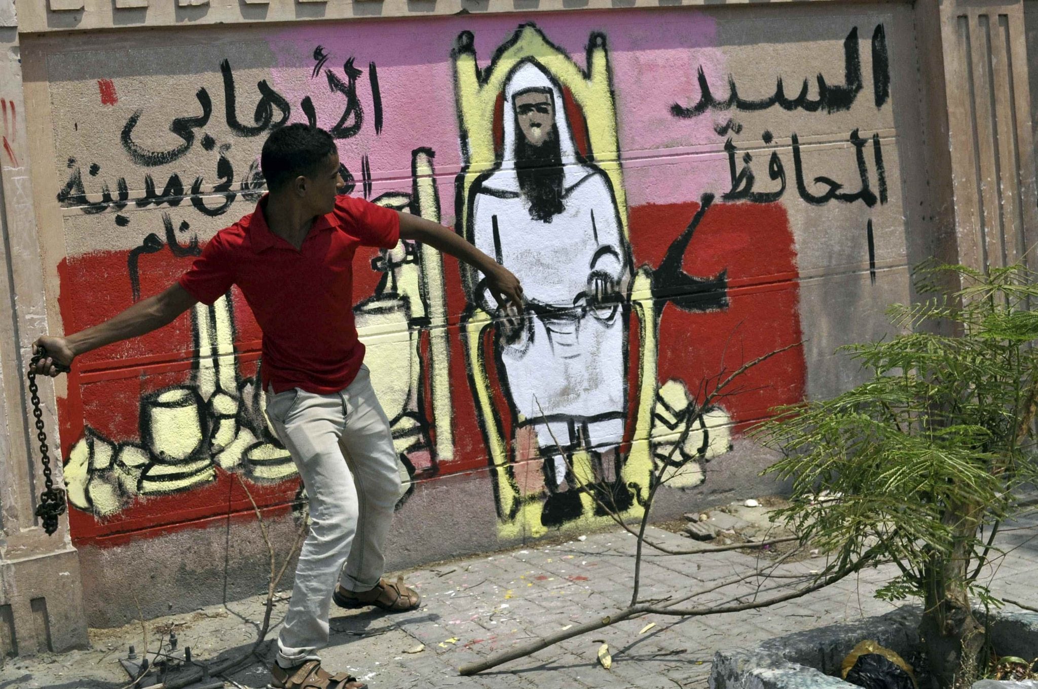 A protester throws a chain next to a graffiti on the wall depicting the newly appointed governor of Luxor Adel Mohamed al-Khayat, as a terrorist.