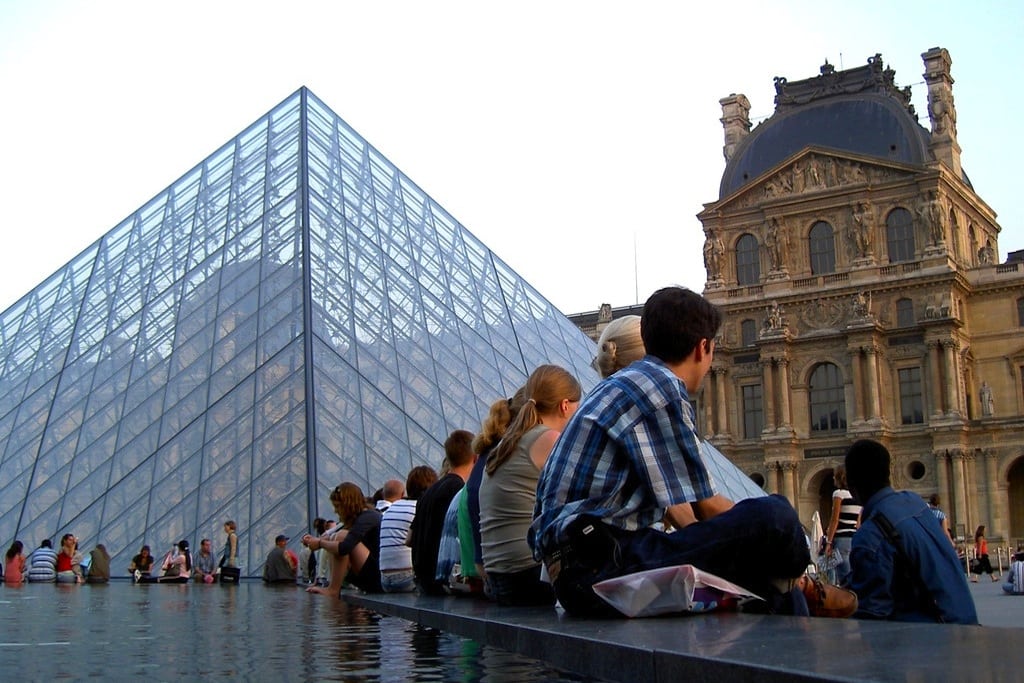 Tourists sit in front of the Louvre in Paris, France. 