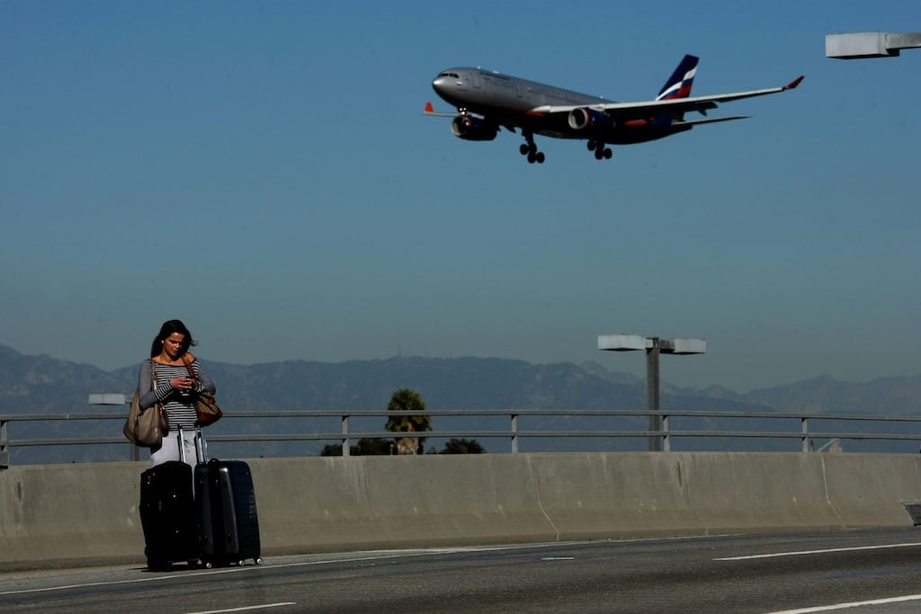 Marcelle Braga stops with her luggage along the entrance way to Los Angeles International Airport as a plane flies overhead on Friday, November 1, 2013. 