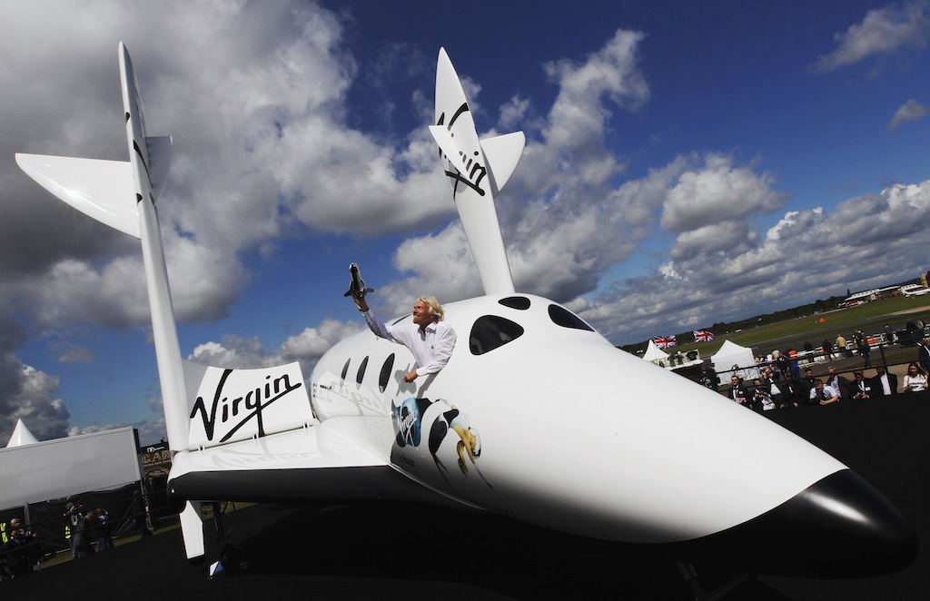 Entrepreneur Richard Branson waves a model of the LauncherOne cargo spacecraft from a window of an actual size model of SpaceShipTwo on display, after Virgin Galactic's LauncherOne announcement and news conference, at the Farnborough Airshow 2012 in southern England in this July 11, 2012 file photo.