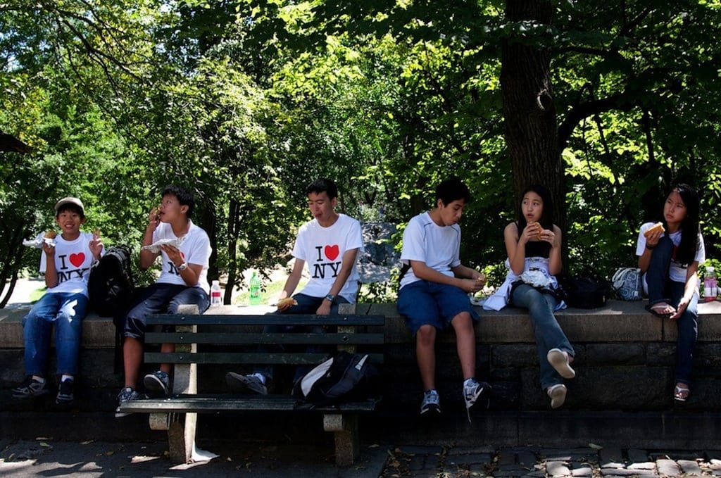 Chinese tourists eat hot dogs and pizza outside of Central Park in New York City.