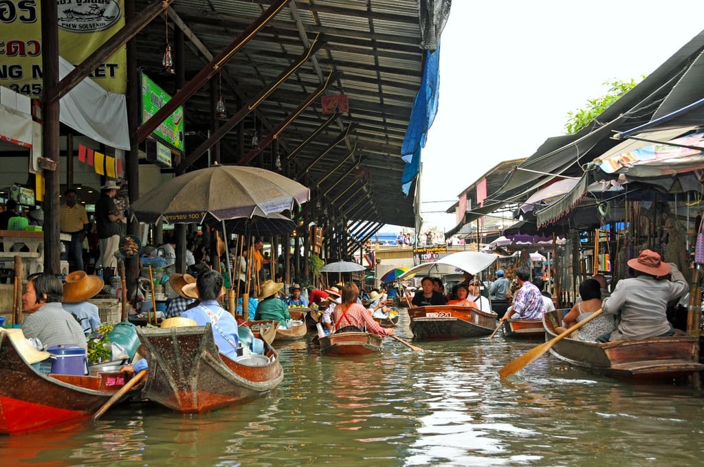 Tourists travel with tour guides down a canal with the floating markets.