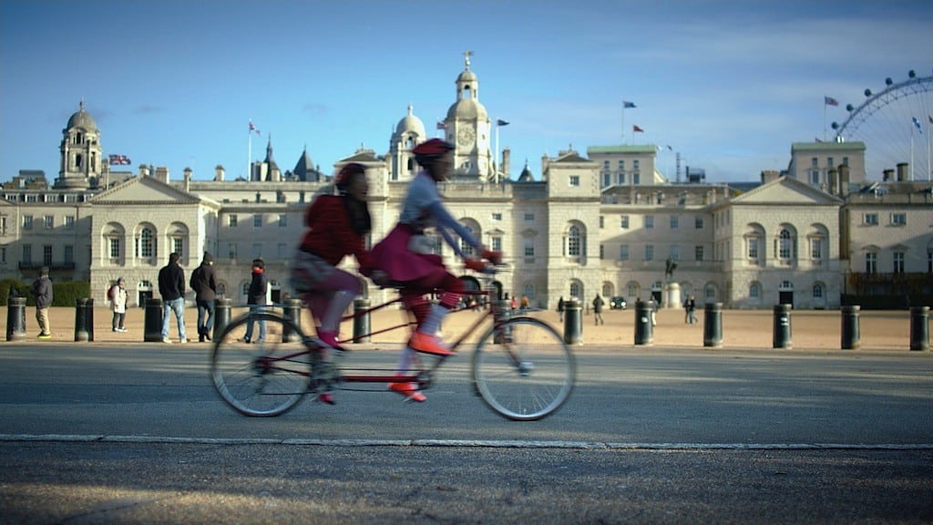 A still of two visitors riding bikes in front of Horse Guard Parade.