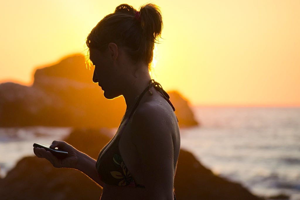 A woman looks at her mobile phone as the sun sets behind her in Montenegro. 