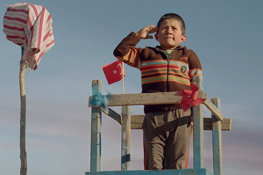 A little boy stands tall and salutes an descending Turkish Airlines jet. 