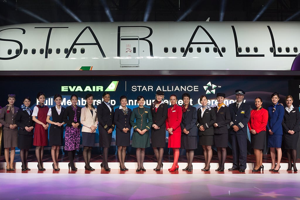 Staff from Star Alliance airlines welcome EVA Air to the Star Alliance family. The staff representatives pose on a stage specially created for the EVA Air joining ceremony, with an EVA Star Alliance branded aircraft as part of the backdrop. 