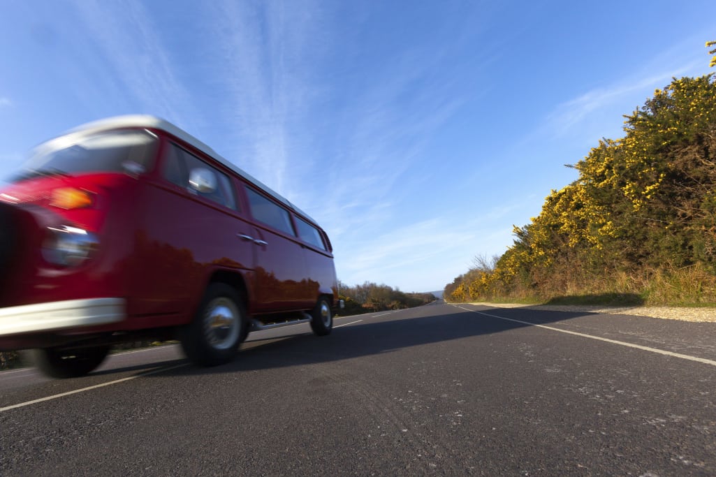 A red camper van drives along an empty highway.