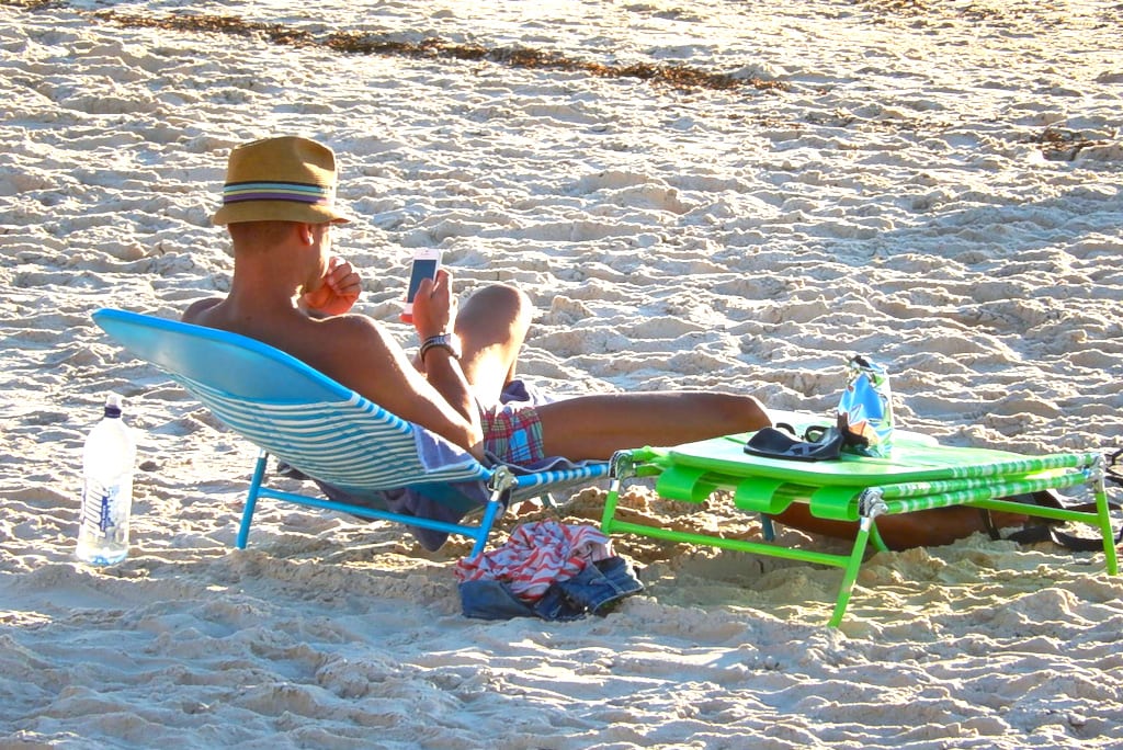 A vacationer glances at his phone on the beach.