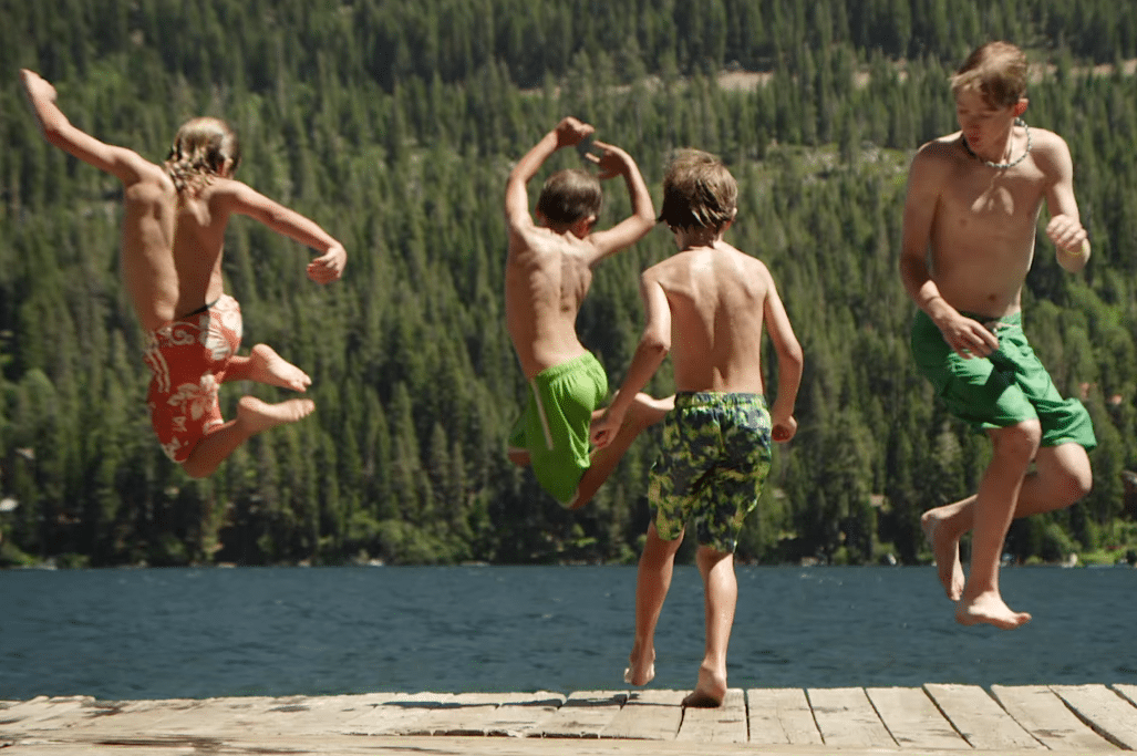 Young boys jump off a dock into a lake.