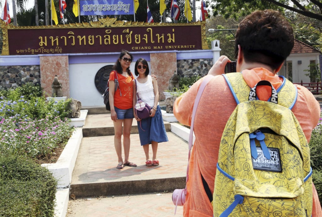 In this photo taken March 30, 2014, Chinese tourists pose for photograph at the main entrance to Chiang Mai University in Chiang Mai province, northern Thailand. 