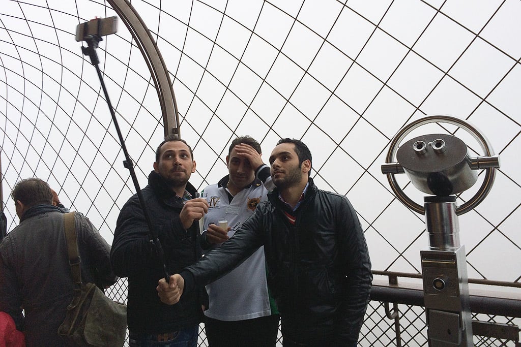 Three friends take a picture with a selfie stick atop the Eiffel Tower in Paris. 