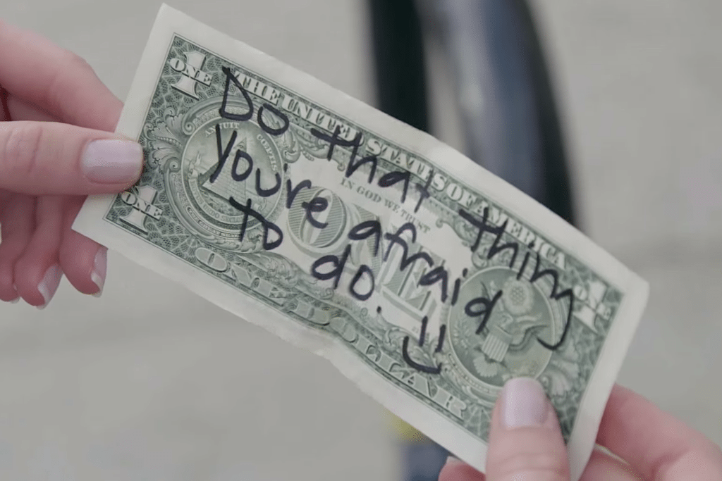 Comedian Erin Foster writes motivational notes on one-dollar bills as part of Airbnb's #OneLessStranger campaign.