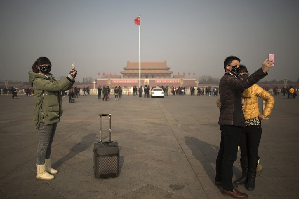 Tourists in masks use mobile phone cameras to snap shots of themselves during a heavily polluted day on Tiananmen Square in Beijing, China, Thursday, Jan. 16, 2014.