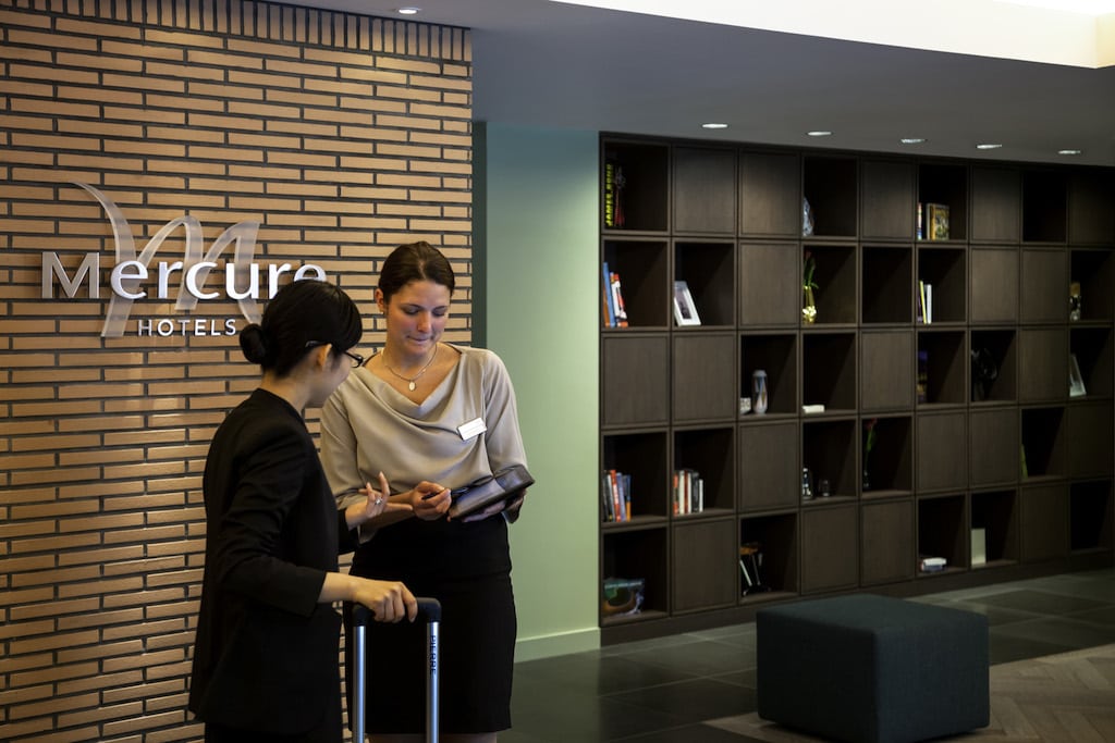 A staff member at a Mercure Hotel greets a guest who has checked in online in advance of her stay. 