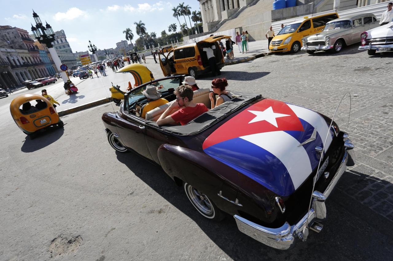 Tourists take a ride in a classic American convertible car with the Cuban national flag painted on the trunk, in Havana, Cuba.