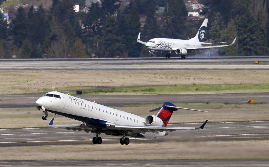 A Delta jet, left, takes-off, as an Alaska Airlines plane lands at Seattle-Tacoma International Airport in SeaTac, Wash. Delta is building Seattle into a gateway to Asia and adding flights on domestic routes long dominated by Alaska. Seattle-based Alaska has responded by adding service. 