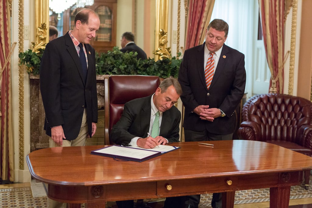 Rep. Bill Shuster (R-Pa.), right, and Rep. Dave Camp (R-Mich.) look on as former House Speaker John Boehner signs The Highway and Transportation Funding Act in 2014.