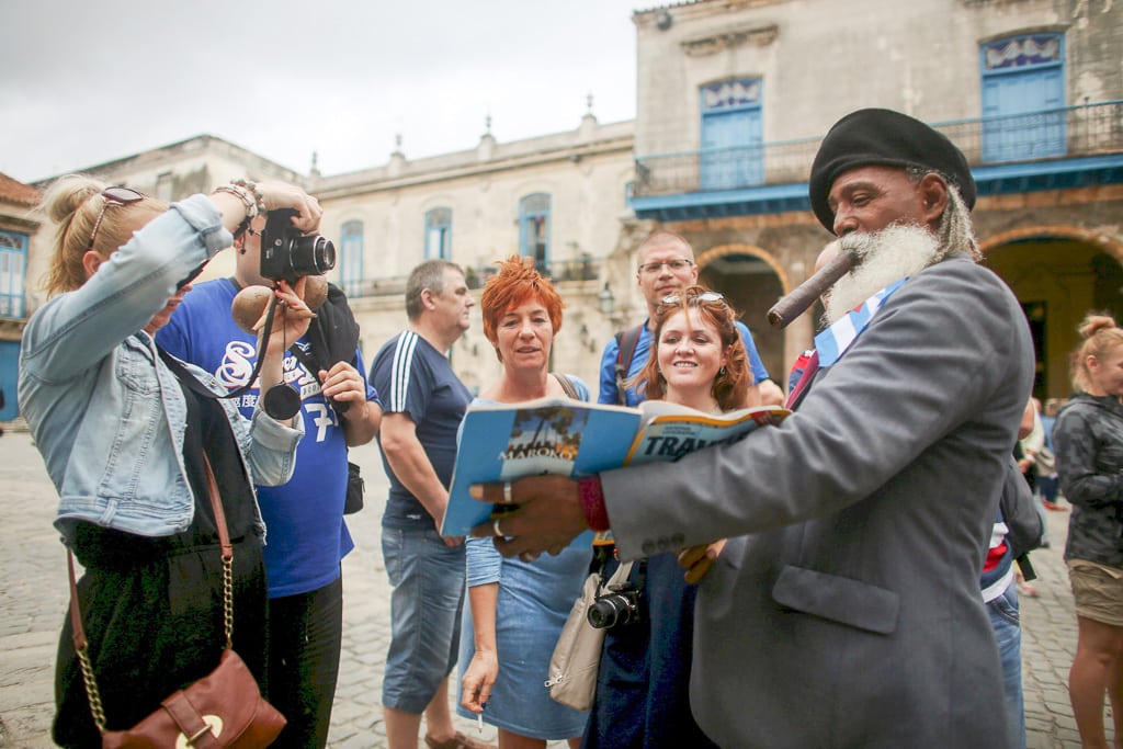 Travel agencies are starting to better educate both young and old agents. Hermenegildo Arensivia, 61, (R), shows pictures of him in a magazine to tourists from Poland in old Havana. 