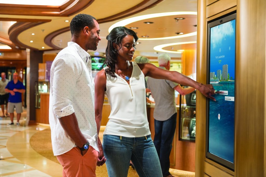This promotional photo shows cruise passengers wearing Carnival Corp.'s new Ocean Medallion and using a portal to get information during their trip. The cruise company is rolling out the wearable technology on Princess Cruises to improve the guest experience.