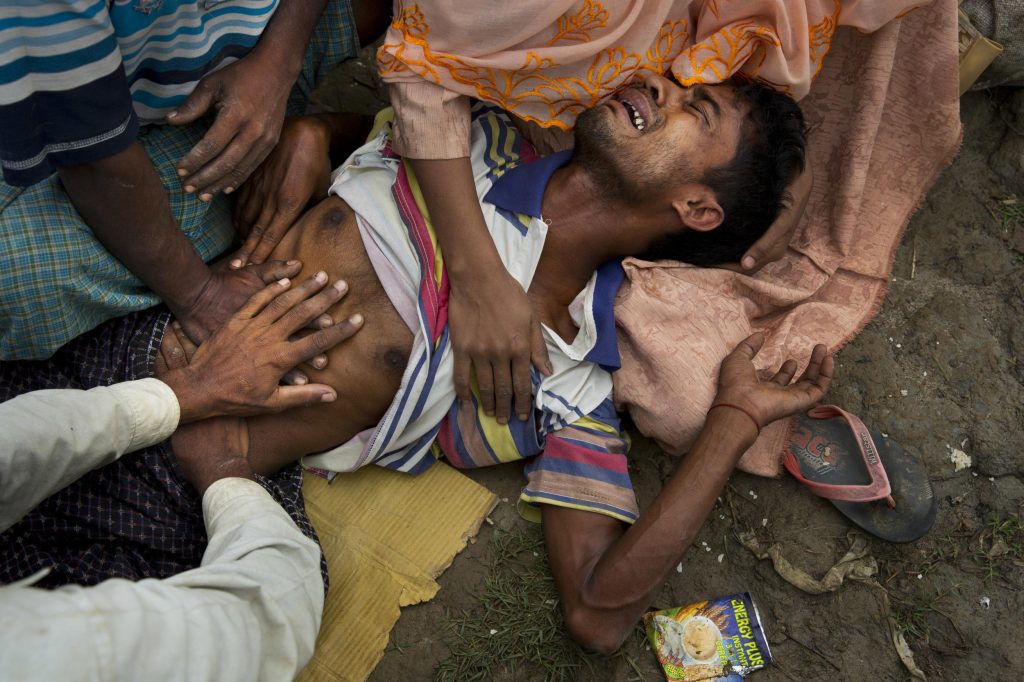In this November 2, 2017 file photo, a Rohingya Muslim man, Muhammed Yunus, 28, who has not eaten for the past three days, grimaces in pain as he along with others wait along the border for permission to proceed to refugee camps near Palong Khali, Bangladesh. More than 600,000 Rohingya from northern Rakhine state have fled to Bangladesh since August 25, when Myanmar security forces began a scorched-earth campaign against Rohingya villages. 