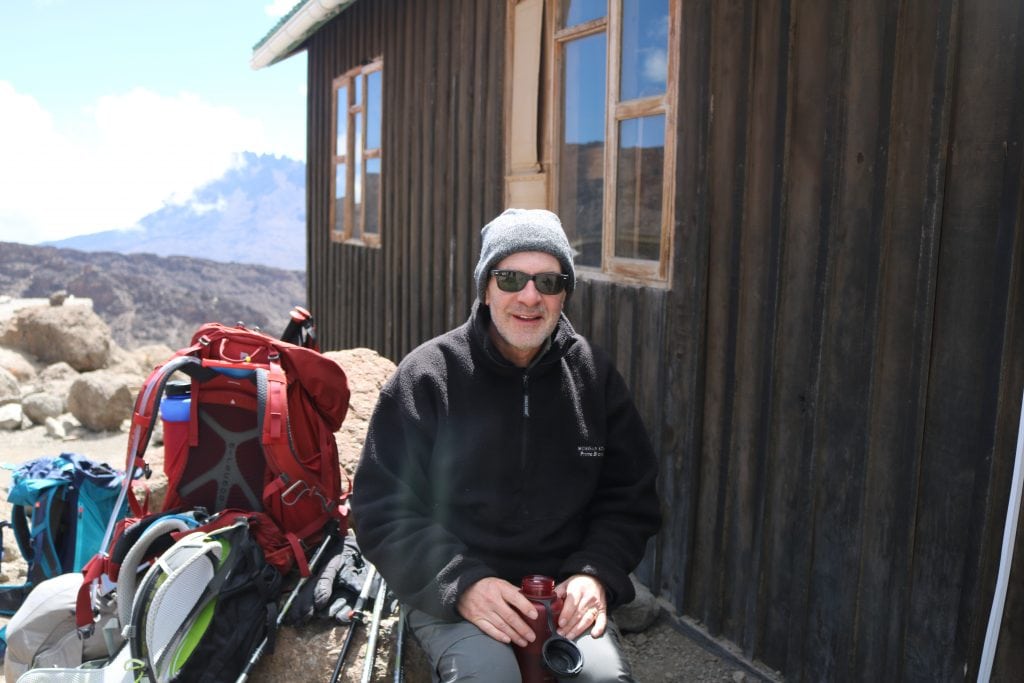 A traveler takes a break while achieving his goal of climbing Mt. Kilimanjaro before his 70th birthday. Luxury adventure travel has become more of a solo pursuit in recent years.