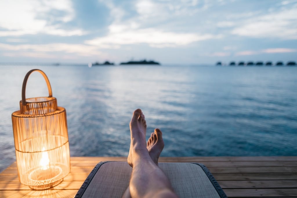 A woman is shown relaxing near the sea. Top hospitality groups including Hyatt and AccorHotels are making guest wellness a priority and are making strategic hires to prove it.
