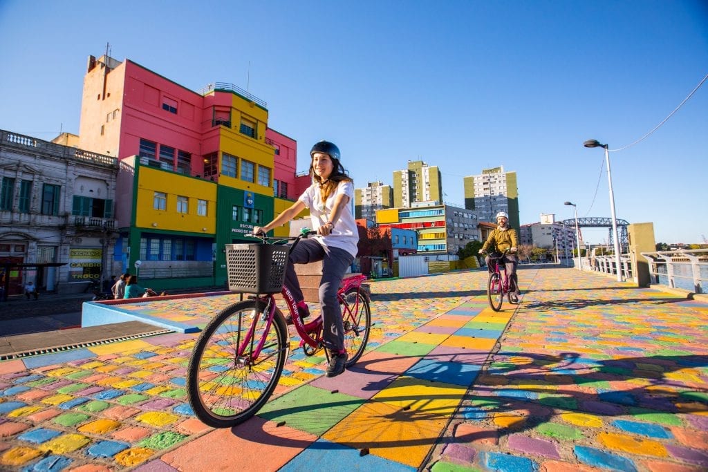 The top image is of someone doing a bicycle tour of Buenos Aires, Argentina, and passing along colorful La Boca district. Inset is an image on an office wall of the logo of Despegar, the largest online travel agency in Latin America, which reported its earnings on Thursday.