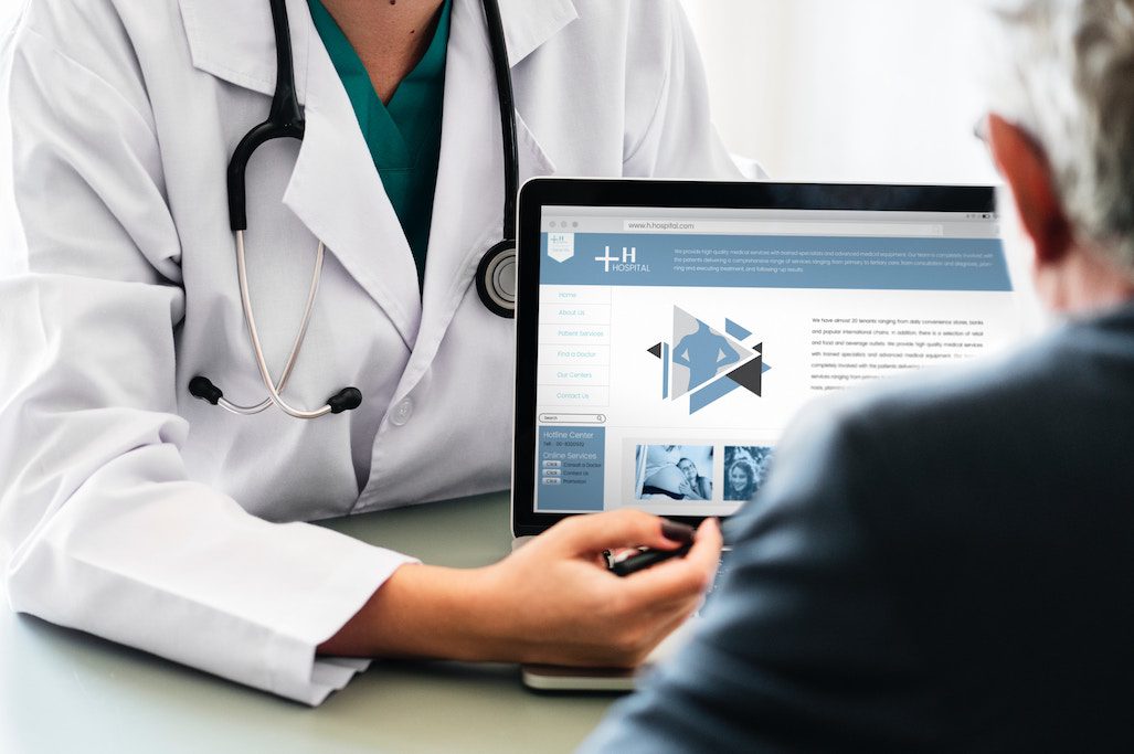 A doctor is showing a patient information on a laptop. Tech startups and legacy brands are redefining how consumers access healthcare and medicine. 
