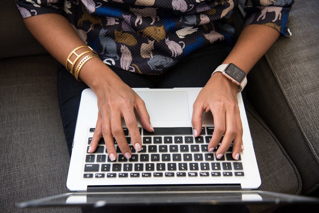 A woman is shown using a laptop wearing a wearable device. As of 2018, 6 million employees worldwide received a wearable device as part of an office wellness program.