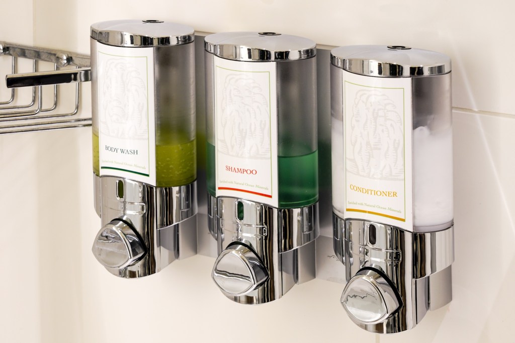 Luxury body wash liquid soap, shampoo and conditioner dispensers boxes on hotel bathroom shower wall.