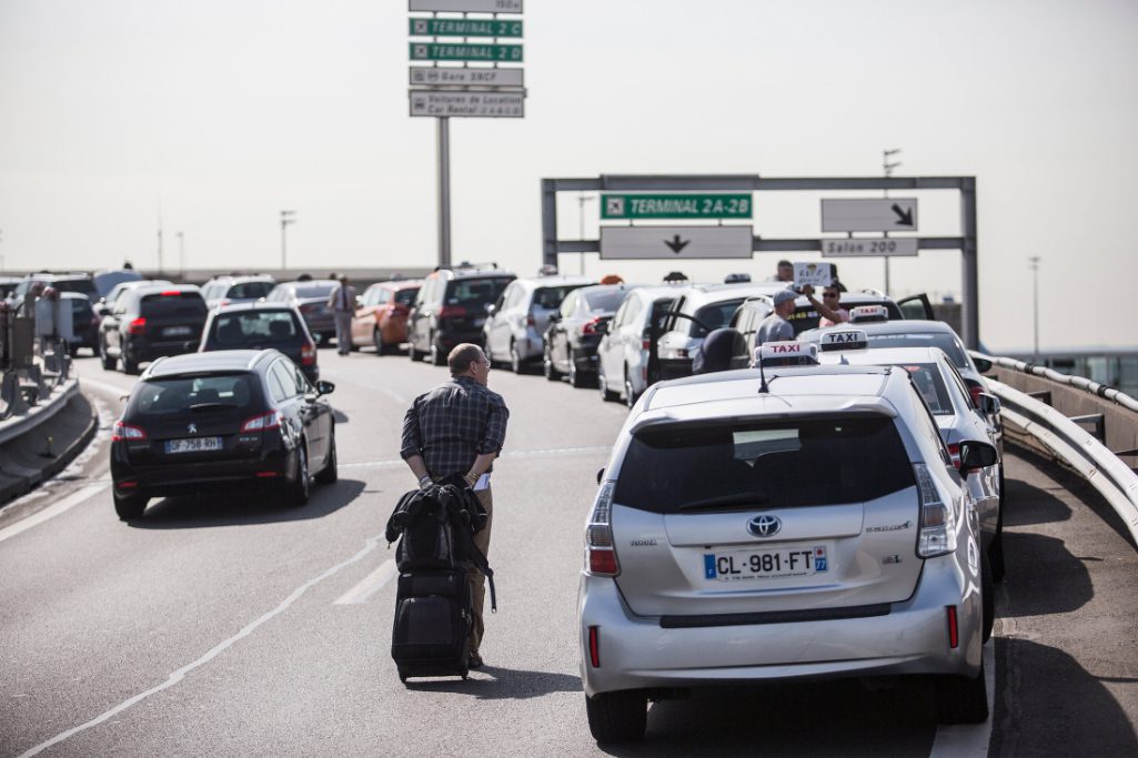 A traveler pulls his luggage past a row of French taxi cabs sat on a road outside Charles de Gaulle airport during a protest against Uber Technologies Inc.'s car sharing service in Roissy, France, on June 25, 2015.